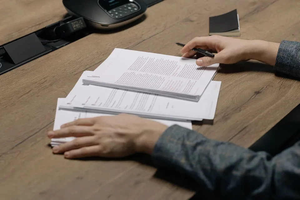 Mains d'un artisan qui parcourent un document papier posé sur une table en bois, illustrant la lecture attentive d'un devis d'agence web avant signature
