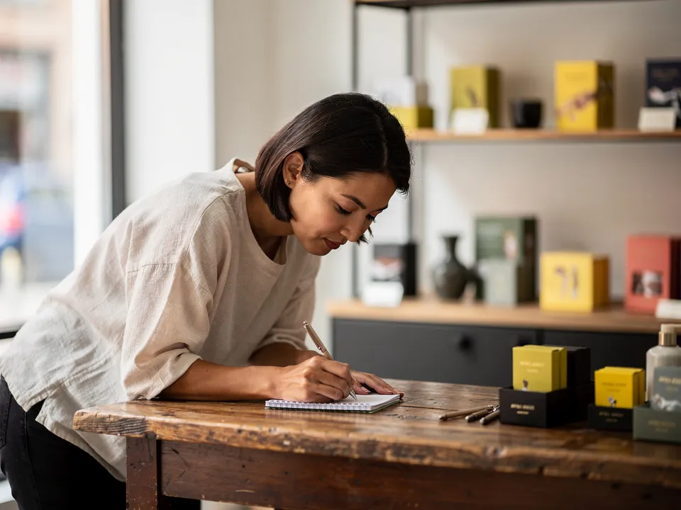 Femme commerçante penchée sur un carnet de notes dans sa boutique, stylo en main, illustrant l'étape de diagnostic avant toute intervention sur un site web d'artisan