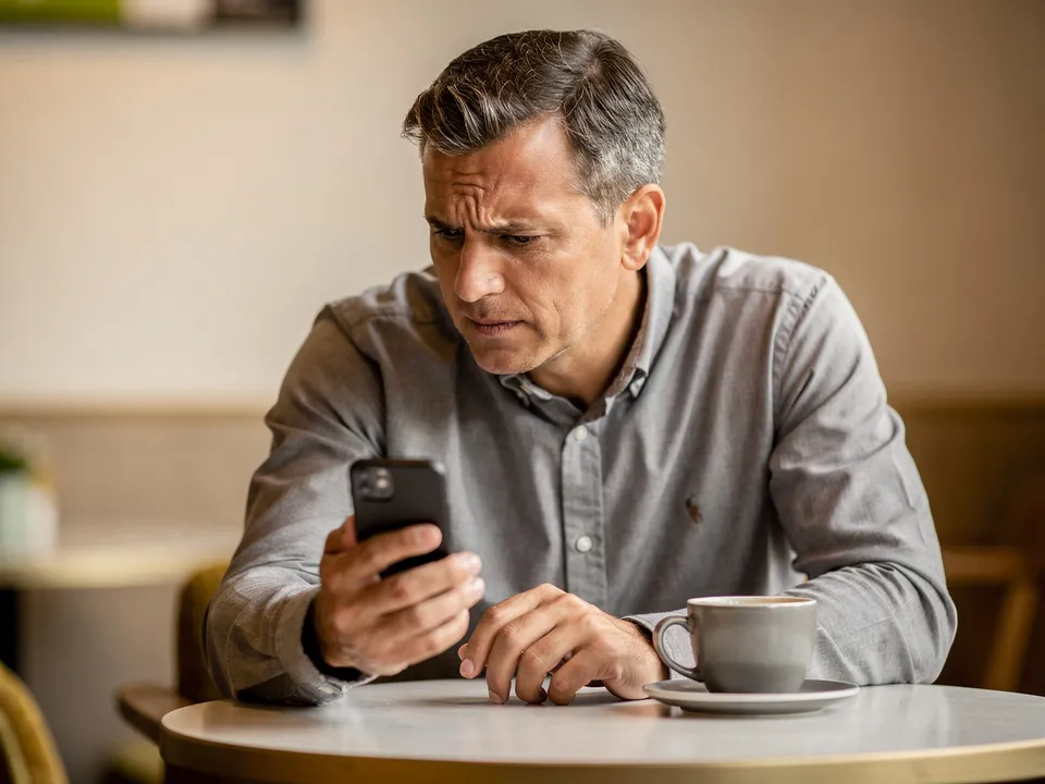 Homme d'une cinquantaine d'années regardant son téléphone avec impatience dans un café, évoquant l'abandon d'un site web trop lent sur mobile